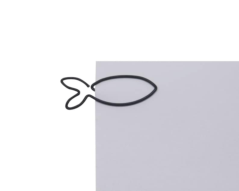 May include: Black metal fish-shaped paperclip holding a sheet of light grey paper.