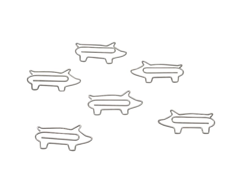 May include: Six silver pig-shaped paper clips. The clips are all the same size and shape, and they are arranged in a random pattern on a white background.