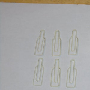 May include: Six white metal bottle-shaped paper clips. The clips are arranged in two rows of three.