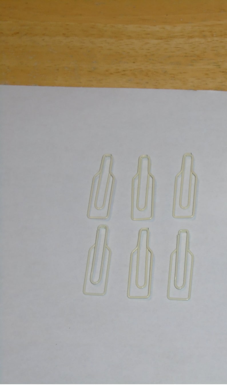 May include: Six white metal bottle-shaped paper clips. The clips are arranged in two rows of three.
