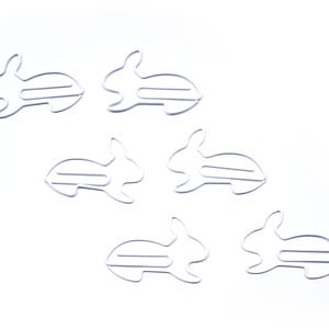 May include: Six white metal bunny-shaped paper clips. The clips are arranged in a staggered pattern on a white background.