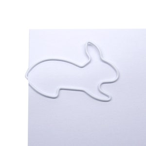 May include: White metal paper clip shaped like a rabbit.