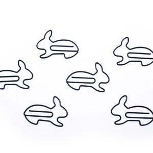 May include: Six black metal paper clips shaped like rabbits. The clips are arranged in a scattered pattern on a white background.