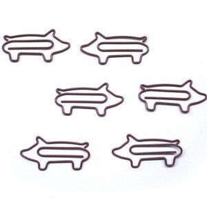 May include: Six brown metal pig-shaped paper clips. The clips are all the same size and shape, and they are arranged in a row.