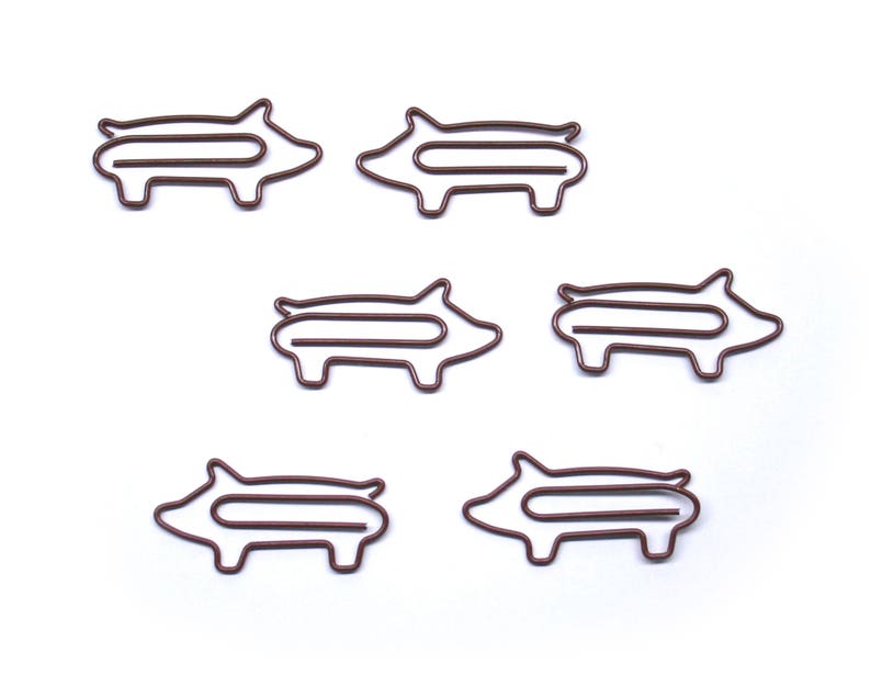 May include: Six brown metal pig-shaped paper clips. The clips are all the same size and shape, and they are arranged in a row.