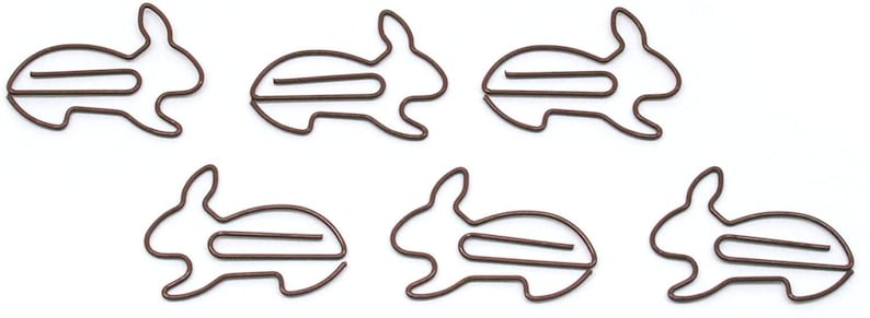 May include: Six brown metal bunny-shaped paper clips. The clips are designed to hold papers together.