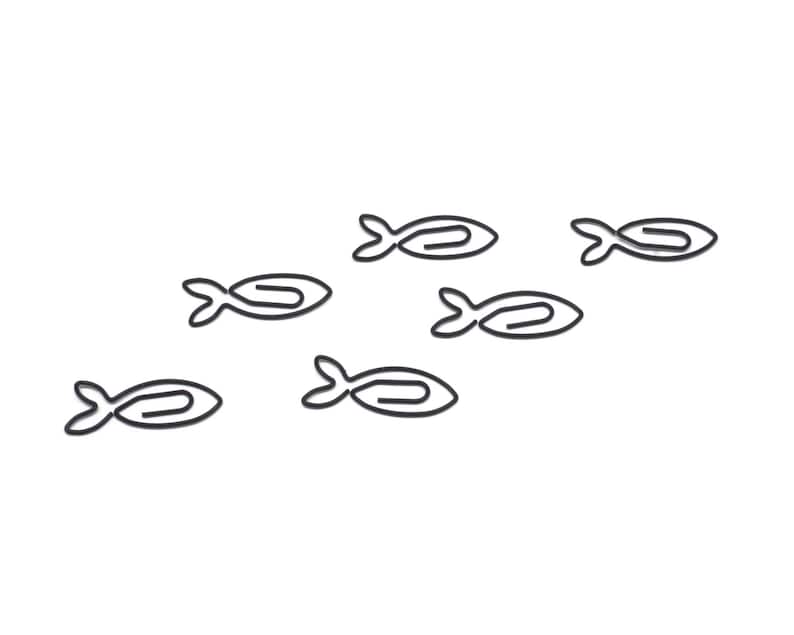 May include: A set of six black paperclip fish, each shaped like a fish with a curved tail and a slightly open mouth. The fish are arranged in a scattered pattern on a white background.