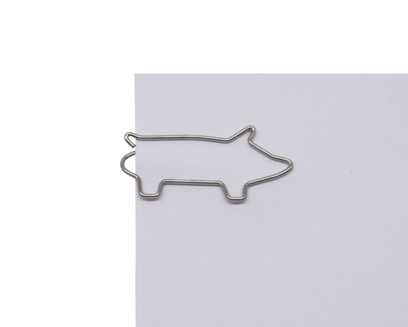 May include: Silver metal pig-shaped paperclip. The paperclip is holding a sheet of white paper.