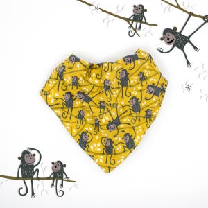 Op de afbeelding: Een gele bandana met een zwart-witte apenprint. De bandana is gevouwen in een driehoekige vorm en heeft een rafelige rand.