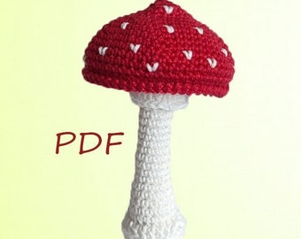 Può includere: Un giocattolo di amigurumi all'uncinetto a forma di fungo con un cappello rosso e macchie bianche, e uno stelo bianco. La parola "PDF" è scritta in rosso sotto il fungo.