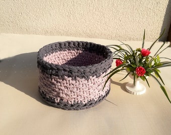 Puede incluir: Una cesta de almacenamiento redonda de crochet con un patrón de rayas grises y rosas. La cesta está hecha de hilo y tiene una textura tejida.