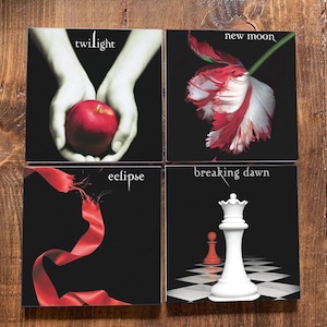 Peut inclure: Quatre couvertures de livres de la saga Twilight. Les couvertures sont noires avec du texte blanc. La première couverture présente une pomme rouge, la deuxième une fleur blanche et rouge, la troisième un ruban rouge et la quatrième une pièce d'échecs blanche.