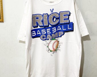 Könnte beinhalten: Weißes T-Shirt mit dem Text "RICE BASEBALL CAMP" in Blau und Grau. Eine Baseball-Grafik durchbricht das Shirt. Das Shirt hängt an einem Holzbügel.