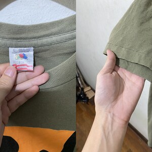 May include: A green t-shirt with an orange and black graphic. The tag says "Fruit of the Loom" and "100% Cotton Made in U.S.A."