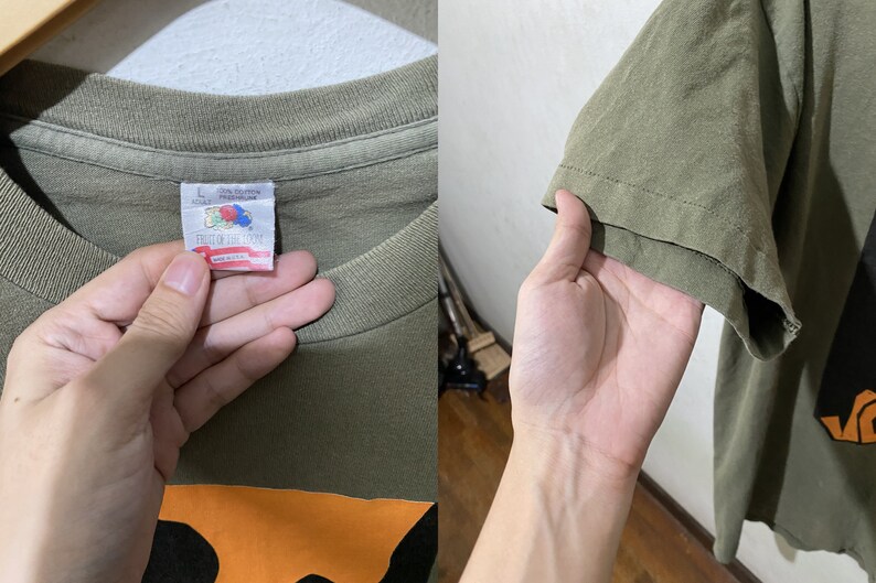 May include: A green t-shirt with an orange and black graphic. The tag says "Fruit of the Loom" and "100% Cotton Made in U.S.A."