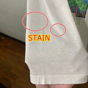 May include: White t-shirt with a colorful graphic print and the text "ANTS: " and "RS". The shirt has two small stains on the sleeve.