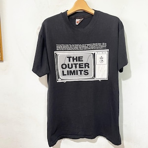 Może przedstawiać: Czarny t-shirt z białym nadrukiem starego telewizora i napisem "THE OUTER LIMITS". Nad telewizorem znajduje się blok tekstu. Koszulka wisi na drewnianym wieszaku.