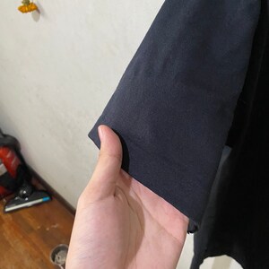 以下が含まれることがあります： 黒いTシャツの袖のクローズアップ。生地は柔らかく、わずかに質感のある表面をしています。