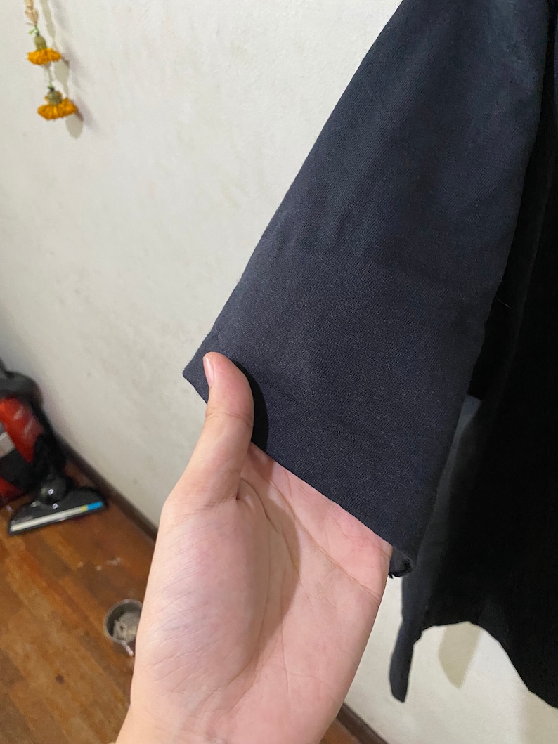 以下が含まれることがあります： 黒いTシャツの袖のクローズアップ。生地は柔らかく、わずかに質感のある表面をしています。