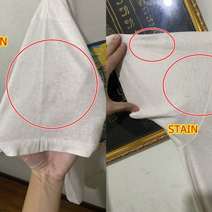 May include: White t-shirt with a stain on the sleeve and a graphic print of a landscape with mountains, a lake, and a sun. The text "STAIN" is written on the shirt.
