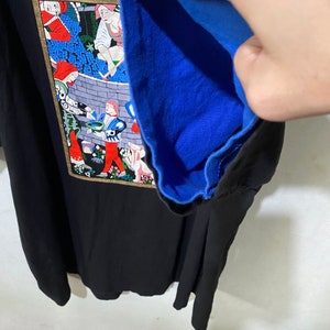 May include: Black t-shirt with a colorful illustration of people working in a vineyard. The illustration is framed in gold and has the text "ROBERT S" at the top. The t-shirt has a blue lining.