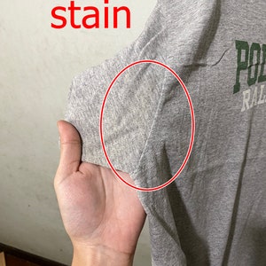 Puede incluir: Camiseta gris con una mancha en la manga. La camiseta tiene texto verde que dice "Polo Ralph Lauren".
