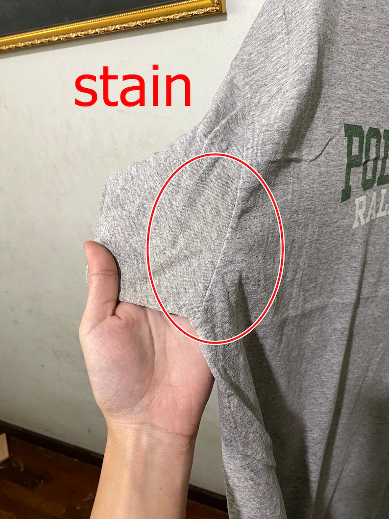 Puede incluir: Camiseta gris con una mancha en la manga. La camiseta tiene texto verde que dice "Polo Ralph Lauren".