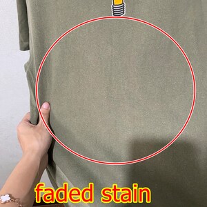 May include: A green t-shirt with a faded stain. The t-shirt features a cartoon lightbulb wearing a top hat and with a mischievous grin. The text "faded stain" is written in red below the lightbulb.