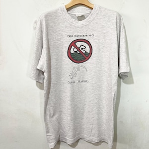 Könnte beinhalten: Hellgraues T-Shirt mit Rundhalsausschnitt und kurzen Ärmeln. Das Shirt zeigt eine Grafik mit dem Text "NO SWIMMING" über einem roten Kreis mit einem durchgestrichenen Schwimmer und einer Krokodil-Illustration. Der Text "Cairns Australia" steht darunter.