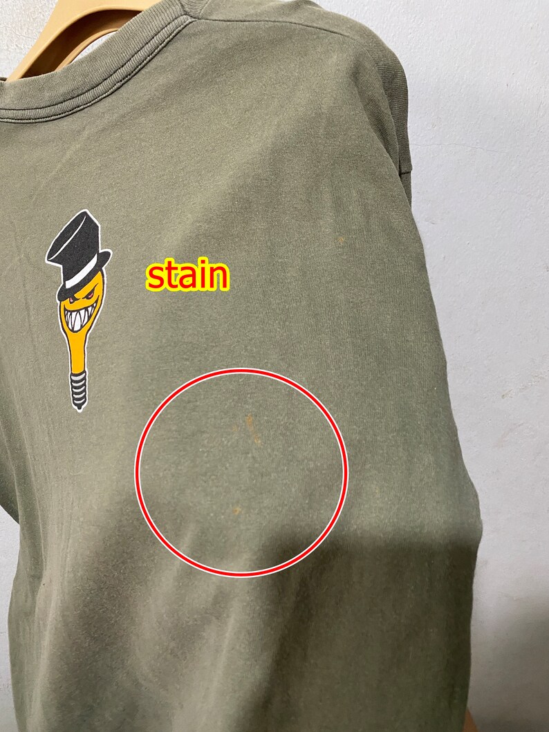 May include: A green t-shirt featuring a cartoon character wearing a top hat. There is a stain on the front of the shirt, circled in red.