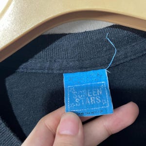 May include: A blue and white tag with the text "Screen Stars" in a white star shape. The tag is attached to a black shirt.