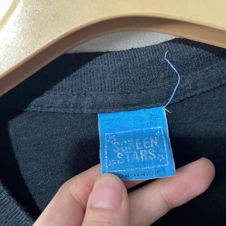 May include: A blue and white tag with the text "Screen Stars" in a white star shape. The tag is attached to a black shirt.