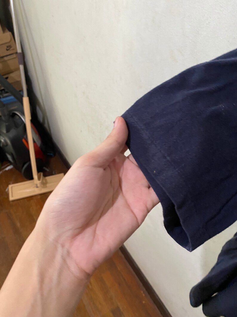 May include: Close-up of the navy blue sleeve of a long-sleeved shirt. The sleeve is folded over and the fabric is smooth.