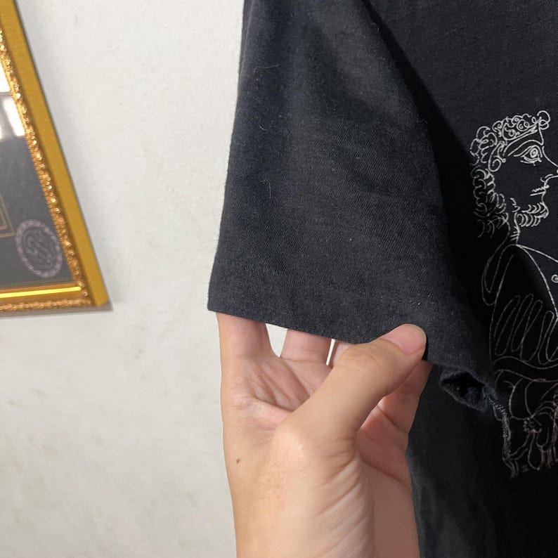 May include: Black t-shirt with a white line drawing of a person's head and shoulders on the right side of the shirt.