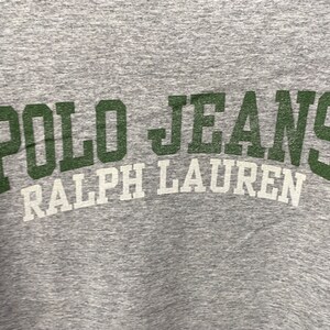 Puede incluir: Camiseta gris con el texto "POLO JEANS RALPH LAUREN" en letras verdes y blancas.