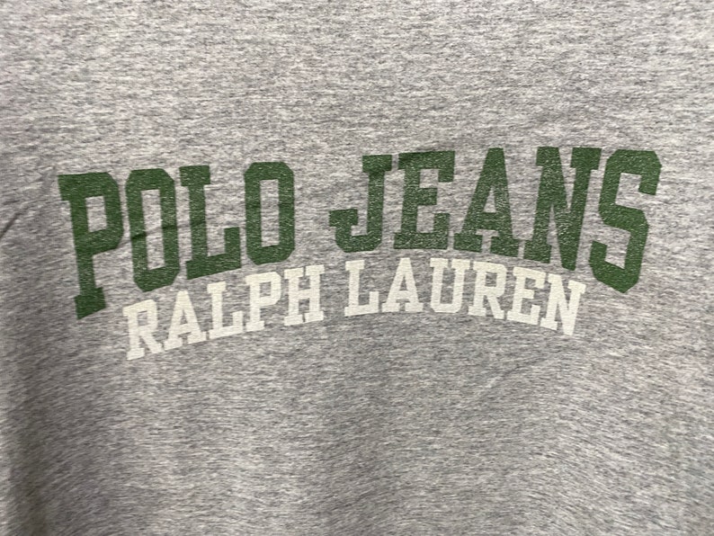 Puede incluir: Camiseta gris con el texto "POLO JEANS RALPH LAUREN" en letras verdes y blancas.