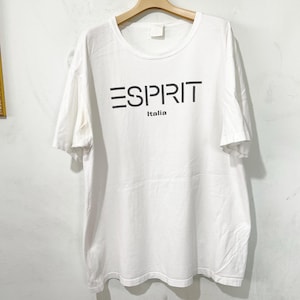 May include: A white short-sleeved t-shirt featuring the word ESPRIT in large black capital letters across the chest, with the word Italia printed in smaller black letters directly underneath the brand name. The shirt has a crew neckline.