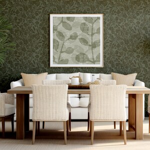 Chic dining room with a wooden table, six wicker chairs, and a white sofa. A large leaf-patterned artwork and green floral wallpaper enhance elegance.