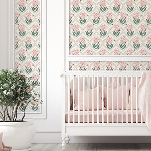Pode incluir: Um ber&ccedil;o branco com roupa de cama rosa e um cobertor rosa macio. A parede atr&aacute;s do ber&ccedil;o apresenta um design de papel de parede floral com flores rosa, folhas verdes e pequenos detalhes em marrom. Uma planta em vaso est&aacute; &agrave; esquerda.