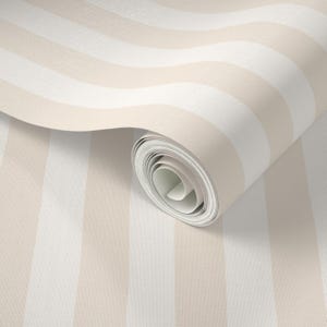 May include: A roll of wallpaper featuring alternating vertical stripes in cream and white. The stripes have a textured appearance, and the roll is partially unrolled, revealing the paper's interior.
