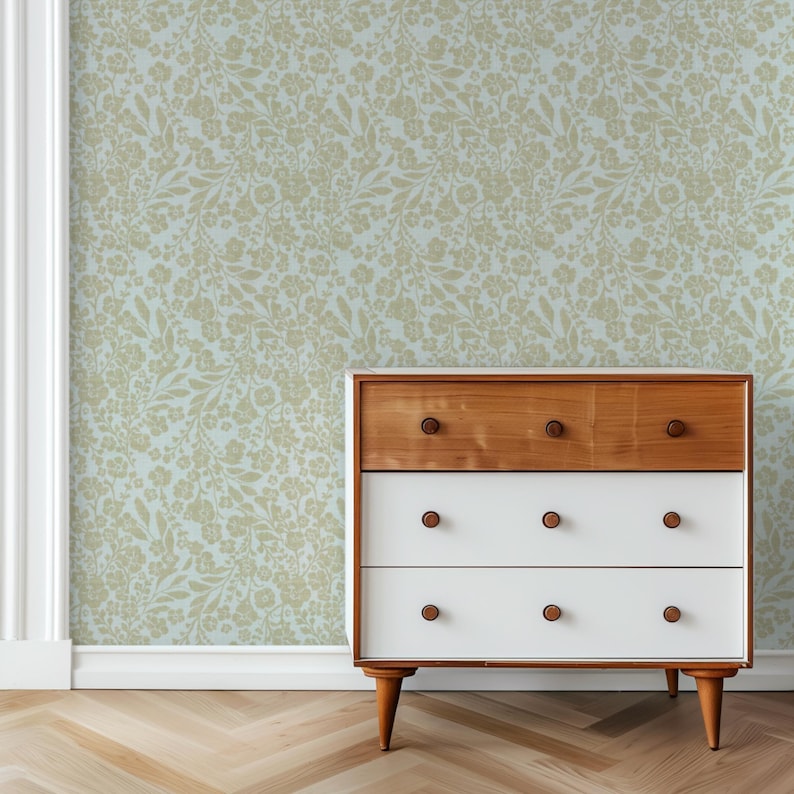 K&ouml;nnte beinhalten: Eine wei&szlig;e Kommode mit vier Schubladen und einer Holzplatte steht vor einer Wand mit einer hellblauen und beigefarbenen Tapetenmuster mit Blumen.