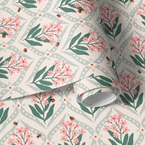 Pode incluir: Papel de parede floral com um padr&atilde;o repetitivo de flores rosa, folhas verdes e joaninhas sobre um fundo creme. O design inclui linhas curvas verde claro com pontos brancos e pequenos detalhes em laranja. Um rolo de papel de parede &eacute; vis&iacute;vel.