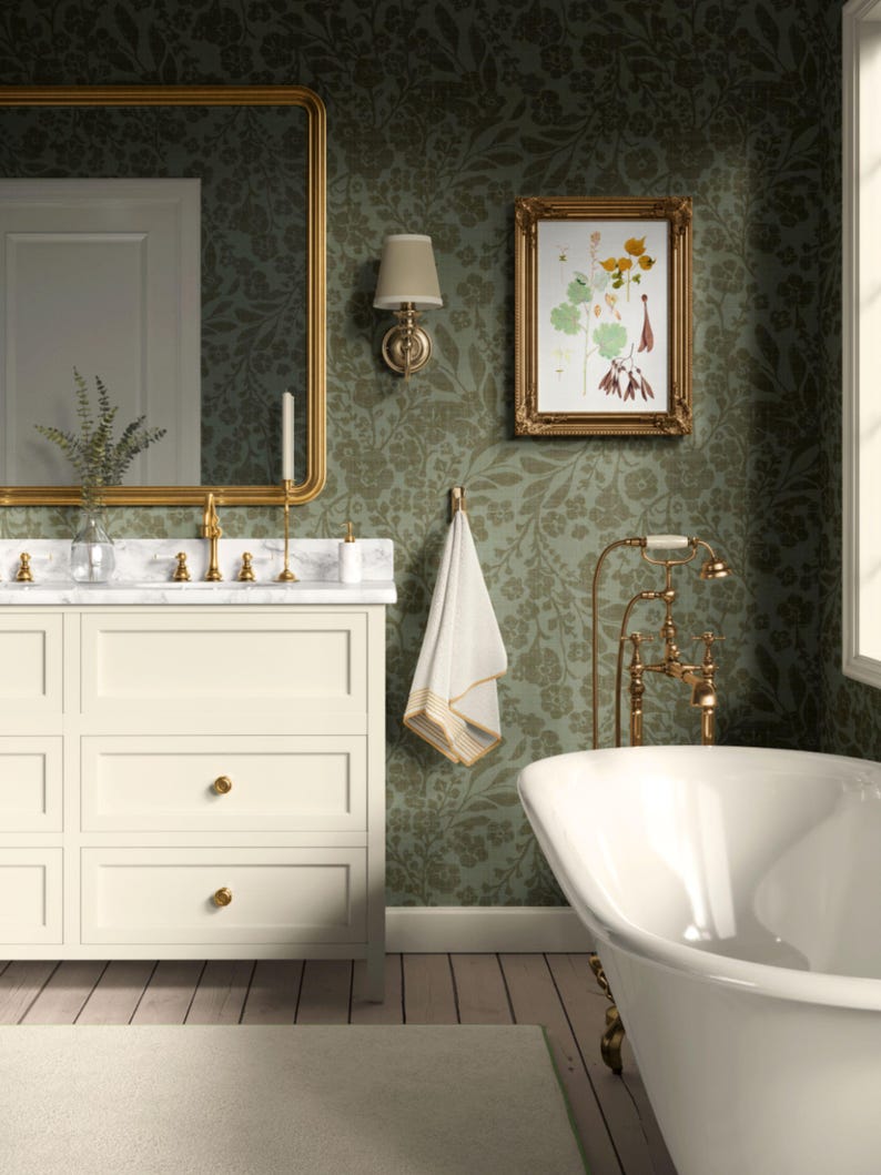 May include: A bathroom featuring a white bathtub, vanity, and framed artwork. The walls are adorned with green floral wallpaper. The vanity has a marble countertop and gold fixtures. A gold-framed mirror hangs above the vanity. A white towel hangs on a gold hook.