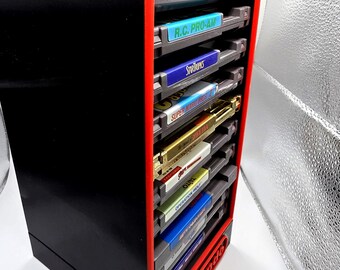 May include: A black and red Nintendo game cartridge storage unit. The unit is rectangular with a red frame and holds several game cartridges. The Nintendo logo is visible on the front. Various game titles are visible on the cartridges.