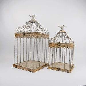 May include: Two decorative birdcages with a distressed white finish. The larger cage is on the left and the smaller cage is on the right. Both cages have a bird figurine on top.