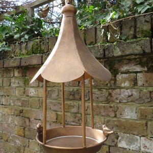 May include: A copper bird feeder with a domed roof and a round base. The feeder is hanging from a chain and has two small bird figures on the sides.