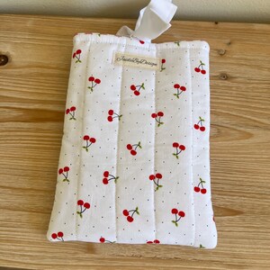 May include: White quilted fabric case with a cherry pattern. The case features red cherries with green stems and leaves, scattered across a white background with small black dots. The case has a white ribbon and the text "JaideByDesign".