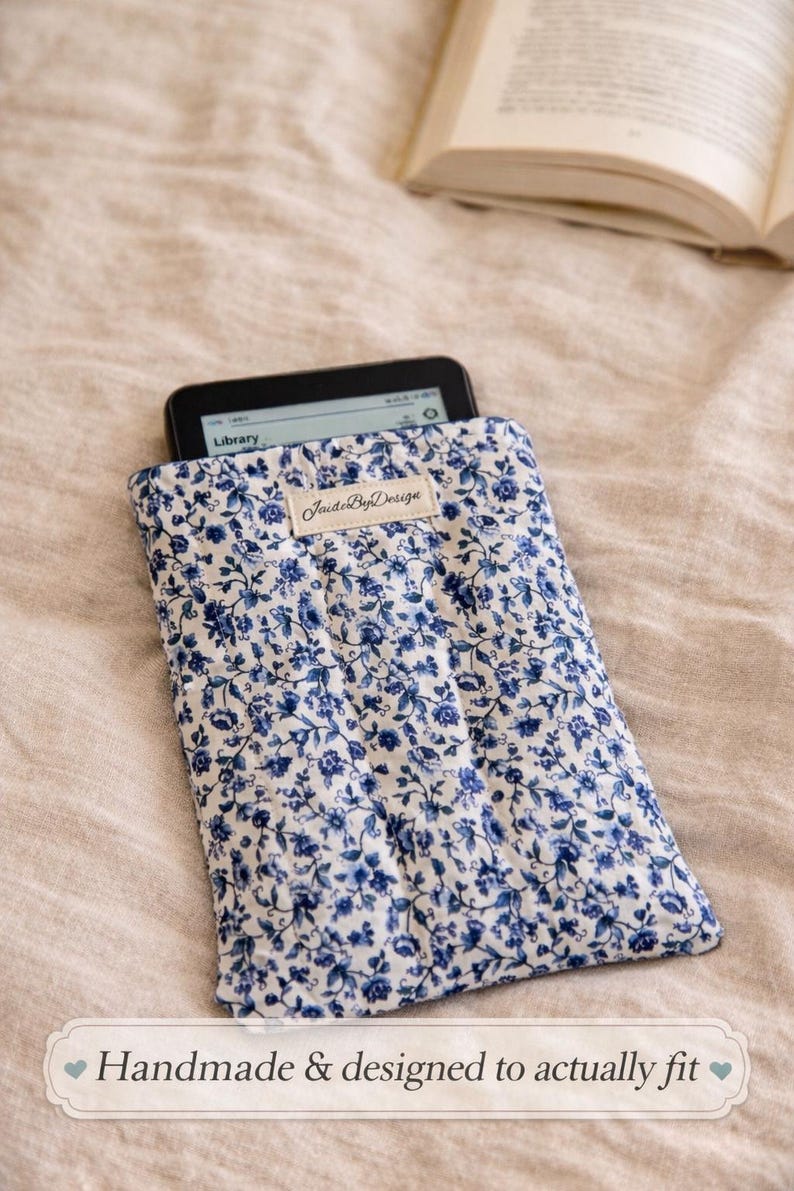 May include: A blue and white floral print e-reader sleeve with an e-reader inside. The sleeve has a label that says "JaideByDesign". The text "Handmade & designed to actually fit" is at the bottom.