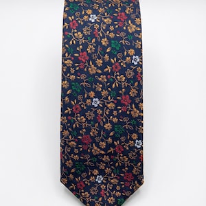 May include: A navy blue tie with a repeating floral pattern. The pattern includes small red, gold, white, and green flowers and leaves. The tie is made of a smooth fabric and is suitable for formal or business attire.