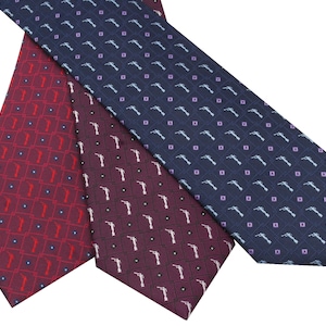 May include: Three neckties in shades of red and navy blue, each patterned with a repeating design of a hand holding a gun. The ties are arranged diagonally, showcasing their different colors and patterns. The background is plain white.